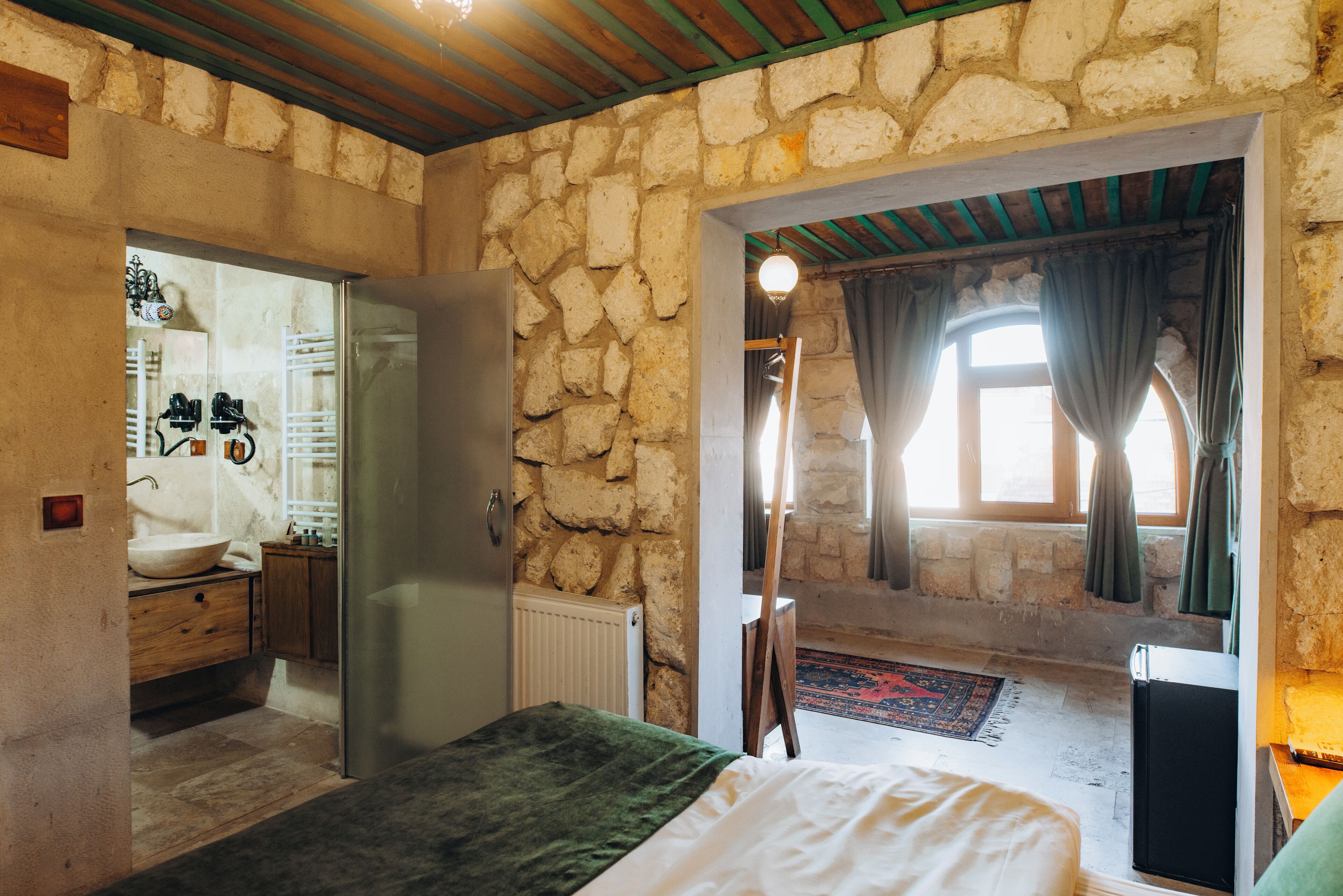 A bedroom with a stone wall, a bed, a dresser, and a bathroom visible through an open door.
