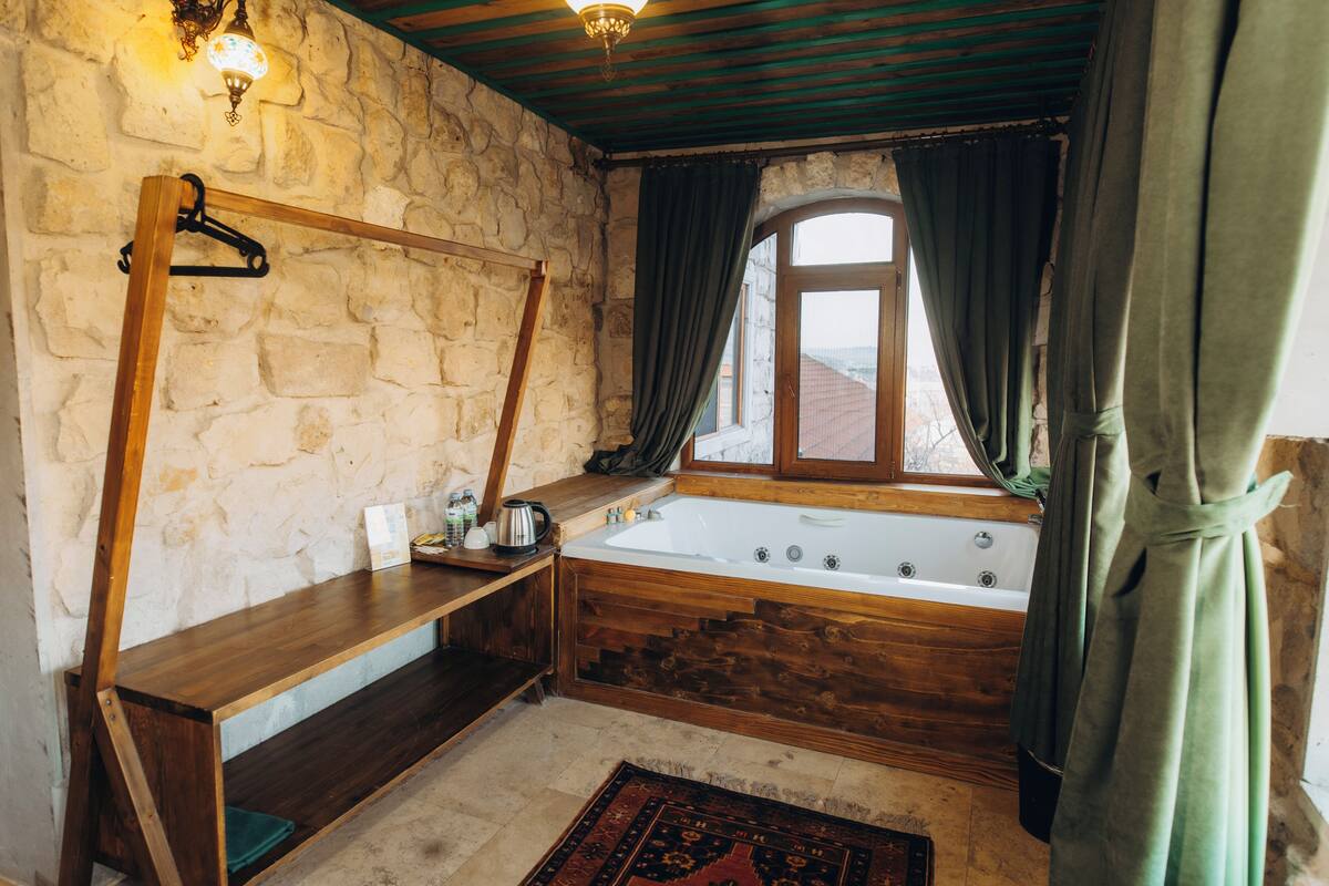 Une salle de bain rustique avec un mur en pierre, une baignoire en bois et une étagère en bois où sont rangés les articles de toilette.