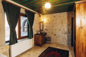 Una habitación con pared de piedra, un armario de madera, un radiador, una alfombra y una ventana con cortinas.