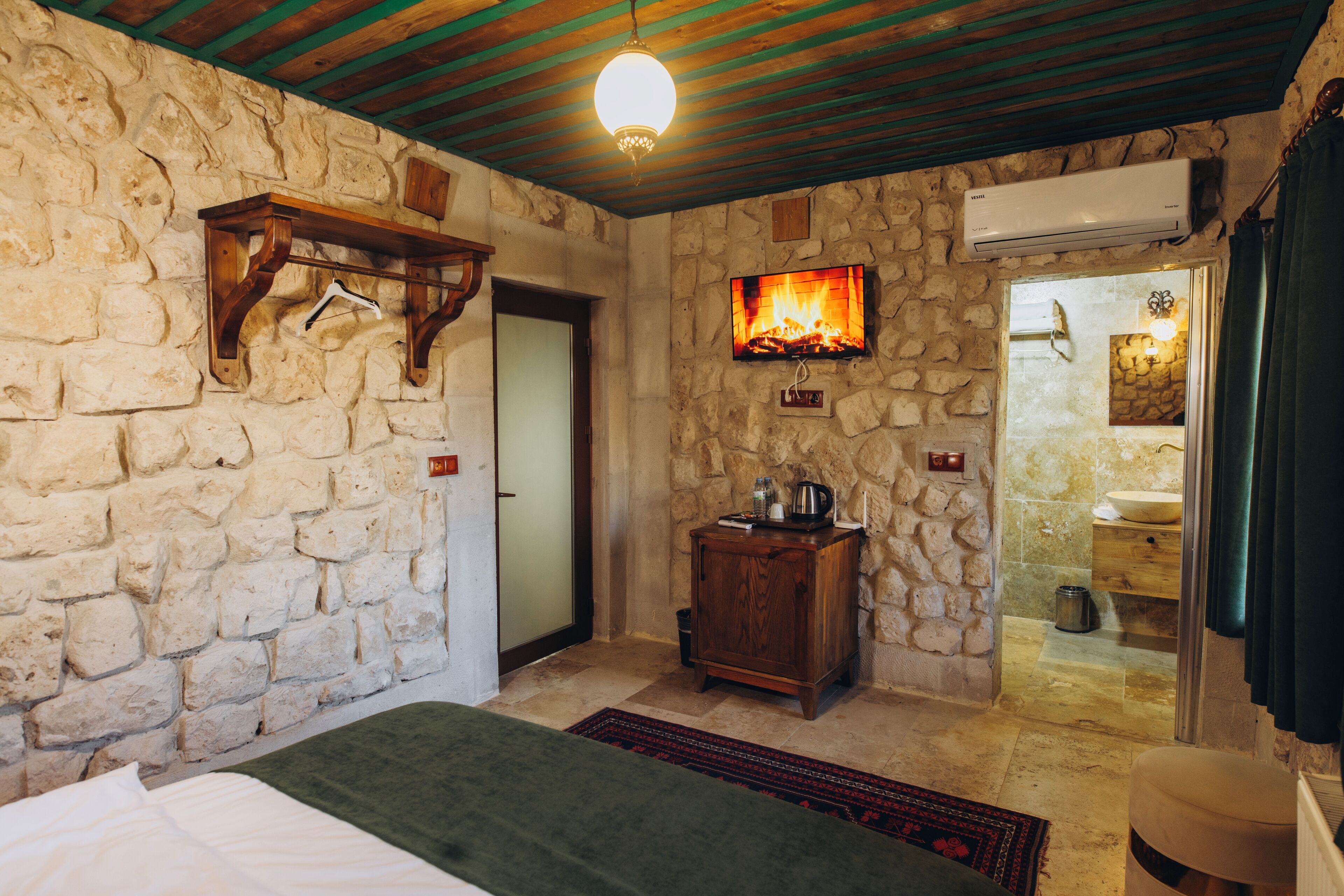 A stone-walled room with a bed, a wooden cabinet, a fireplace, and an air conditioning unit.