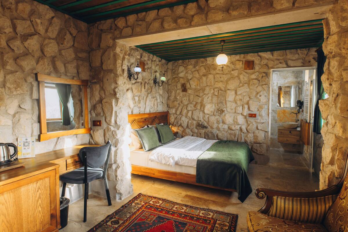 Une chambre aux murs de pierre, avec un lit en bois, un bureau et une chaise, et un tapis à motifs.