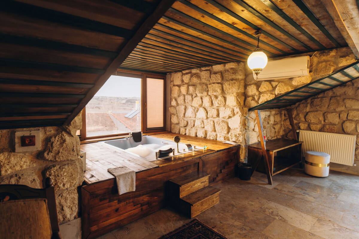 Une salle de bain rustique aux murs de pierre, avec une baignoire en bois, un banc en bois et un lavabo en pierre.