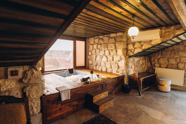 Un baño rústico con paredes de piedra, una bañera de madera, un banco de madera y un lavabo de piedra.