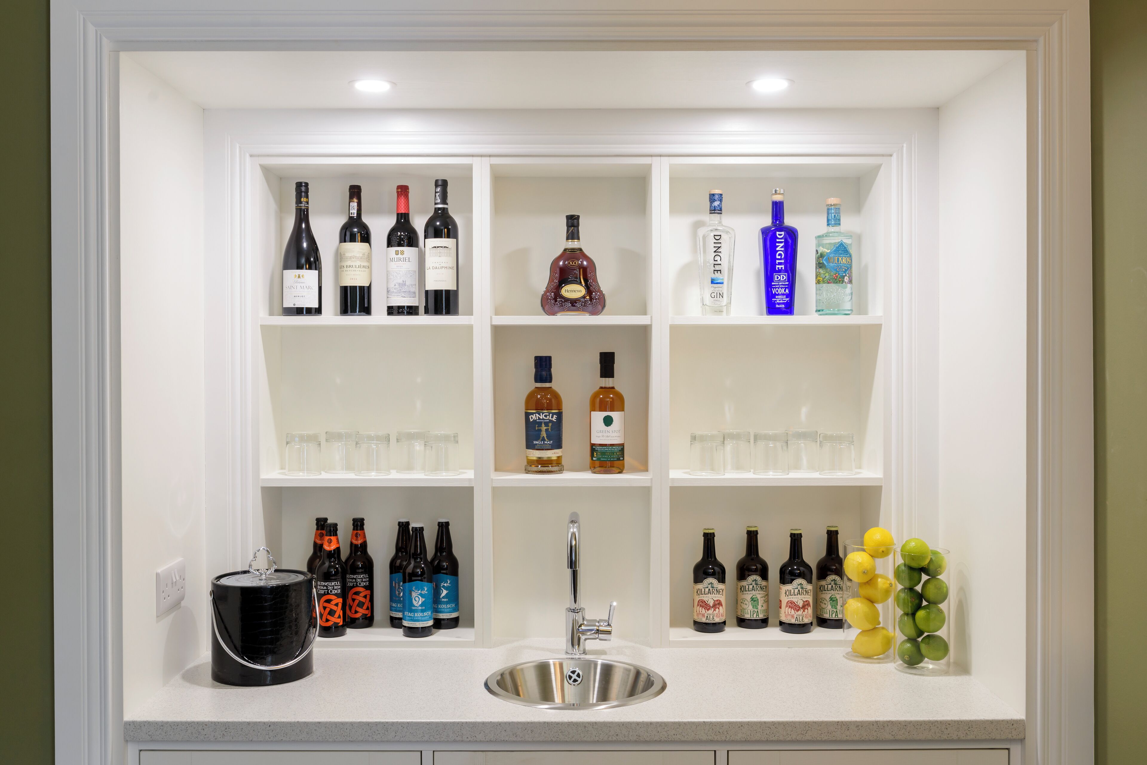 A kitchen with a built-in wine and liquor storage area, a sink, and various bottles and glasses.