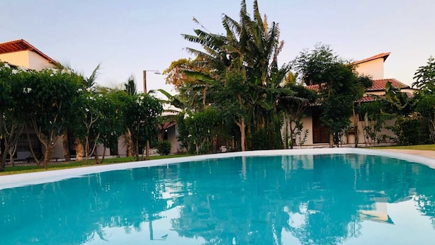 En klar, blå swimmingpool omgivet af frodig vegetation og bygninger med røde tegltage.