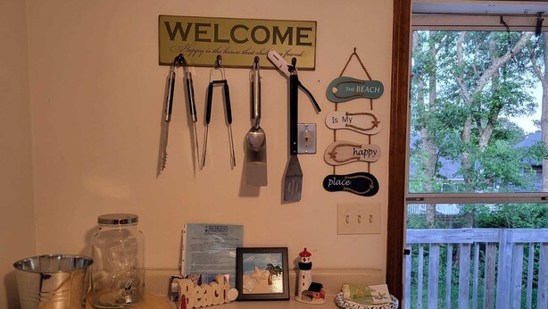 Una encimera de cocina con un letrero de bienvenida, utensilios de cocina, un marco con una foto y decoración con temática playera.