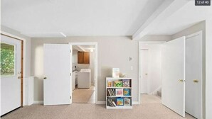 Un pasillo con puertas blancas, suelo alfombrado y una pequeña estantería con libros.