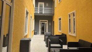 A corridor with yellow walls, a tiled floor, and outdoor seating with black furniture. - Guest House Acácias Rubras (Ferreira do Zezere)