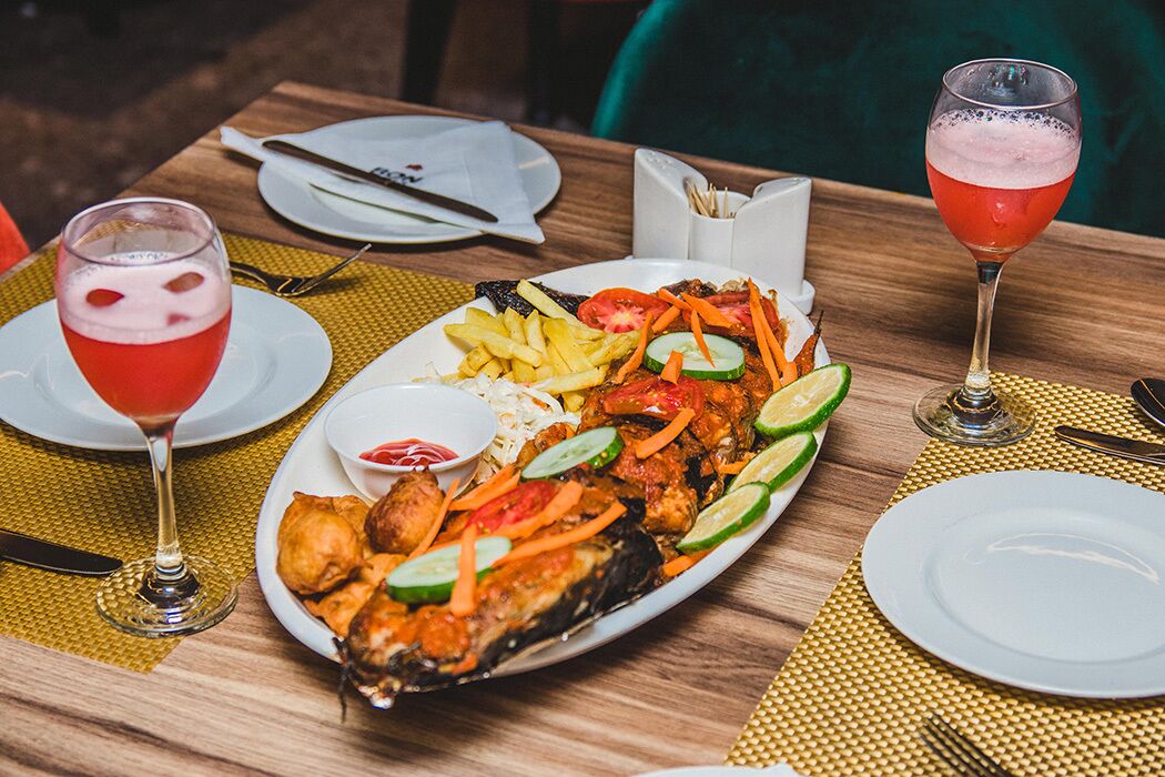 Een eettafel met een bord gegrilde vis, frietjes en groenten, vergezeld van twee drankjes.