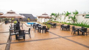 Un espacio al aire libre con mesas, sillas, piscina y sombrillas.