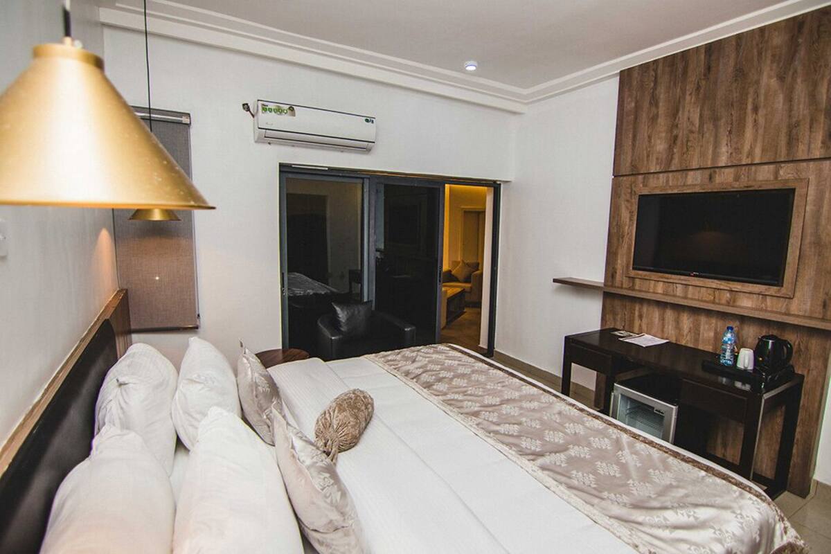 A hotel room with a bed, a desk, a TV, an air conditioning unit, and a sliding door.