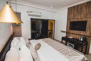 A hotel room with a bed, a desk, a TV, an air conditioning unit, and a sliding door. - Loomzy Suites and Apartments (Lekki)