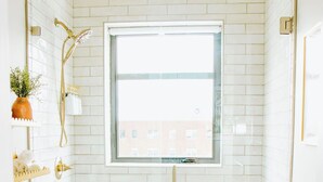 Ein kleines Badezimmer mit weißen Fliesen, einem Fenster, einer Toilette und einer Dusche.