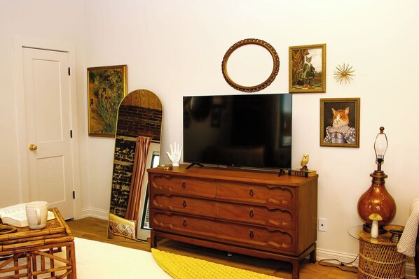 A room with a wooden dresser, a flat-screen TV, a mirror, and various framed pictures on the wall.
