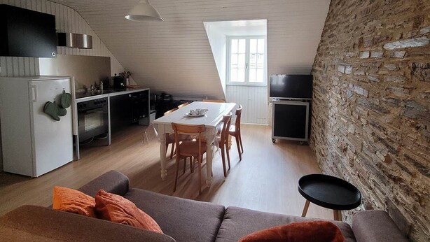 A modern loft apartment with a dining area, kitchen, and a cozy seating area with a sofa and ottoman.