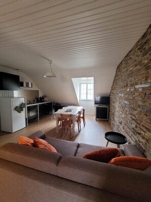 A modern loft apartment with a dining area, kitchen, and a cozy seating area with a sofa and ottoman.