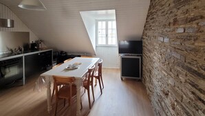 A modern kitchen with a dining area, featuring a sloped ceiling, a brick wall, and a large window.