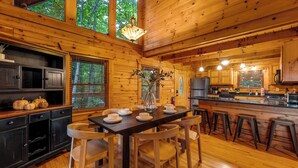 A wooden cabin interior with a dining table set for four, wooden floors, and a kitchen area with modern appliances. - Smoky Mtn Cabin | Hot Tub | Sleep 12 | Pets | View (Gatlinburg)