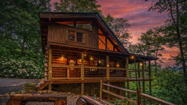 A log cabin with a balcony, surrounded by trees and a stone foundation. - Smoky Mtn Cabin | Hot Tub | Sleep 12 | Pets | View (Gatlinburg)