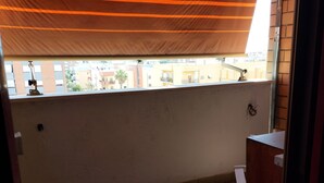 Een balkon met een gestreepte zonnewering, uitzicht op gebouwen en een houten deur.