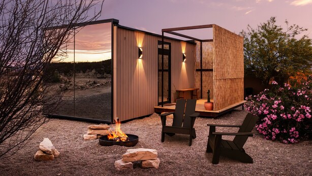 Un espacio exterior moderno con una fogata, zona de estar y una estructura de madera.