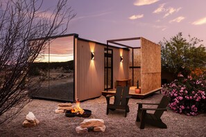 Un espacio exterior moderno con una fogata, zona de estar y una estructura de madera.