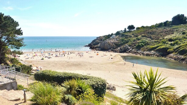 A beach with a rocky cliff, a clear sky, and a calm sea.