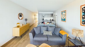A modern living room with a grey sofa, wooden console, and a dining area with a table set for two.