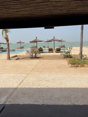 A beachside pool area with lounge chairs and umbrellas, a clear view of the sea, and a thatched roof structure. - CASA COCO II (Nianing)