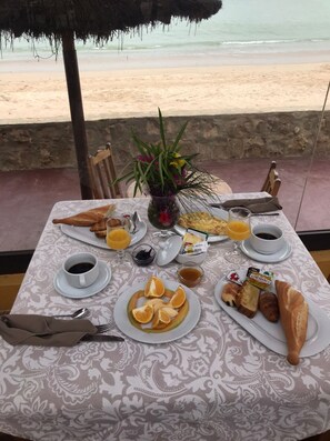 A table set with breakfast items including croissants, orange slices, and coffee, overlooking a beach. - CASA COCO II (Nianing)