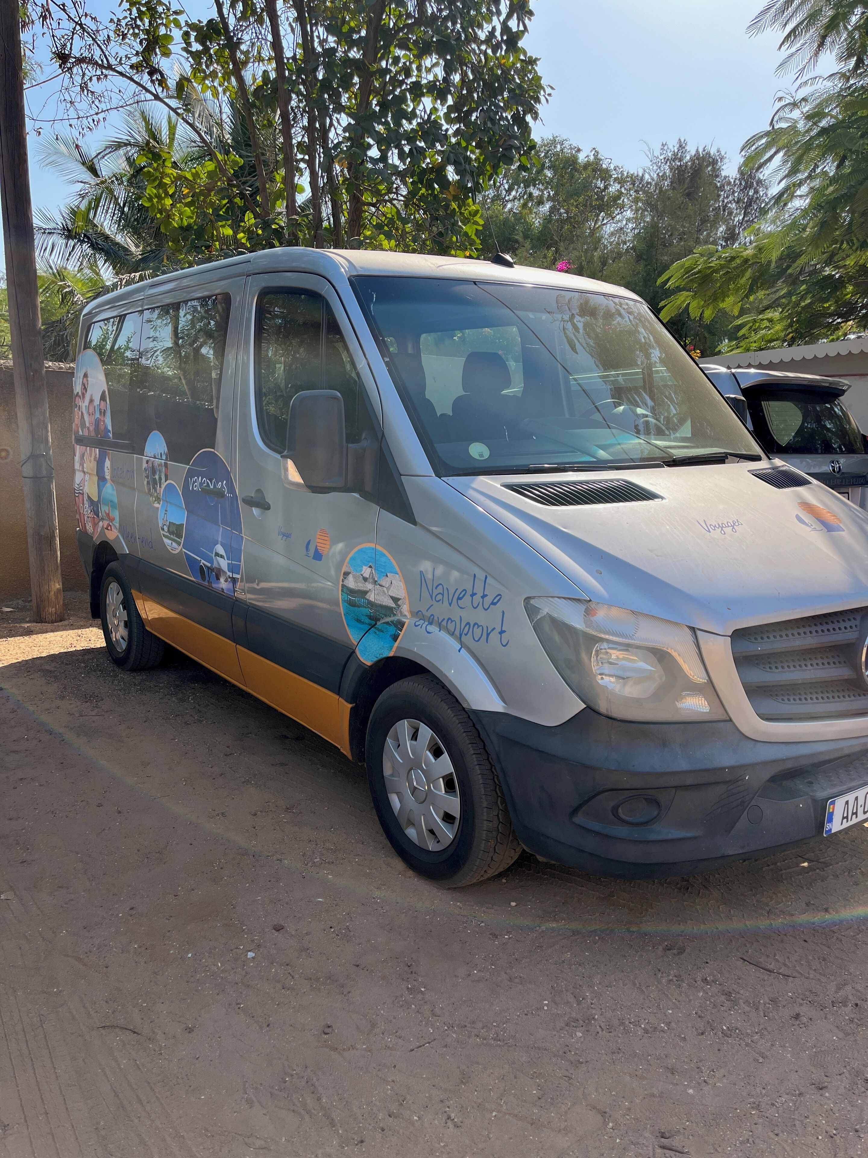 A van parked on a dirt road with a side advertisement for Navette Airport.