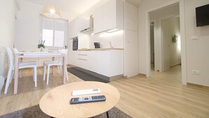 Une cuisine moderne avec des meubles blancs, un coin repas comprenant une table et des chaises, et une télécommande posée sur une table basse.