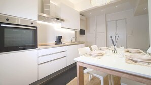 Une cuisine moderne avec des meubles blancs, un four encastré et un coin repas avec une table blanche dressée pour quatre personnes.