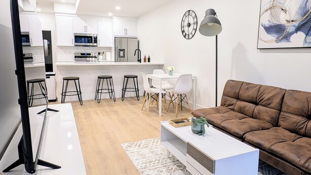 A modern living room with a brown sofa, a white coffee table, and a TV stand. - Modern 2BR Suite | Private Patio | 5 Min Downtown/Zoo/Stampede | Central & Safe (Calgary)