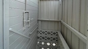 Un espace extérieur étroit et clos, doté d’un toit en métal, de murs blancs et d’une grille de drainage au fond.