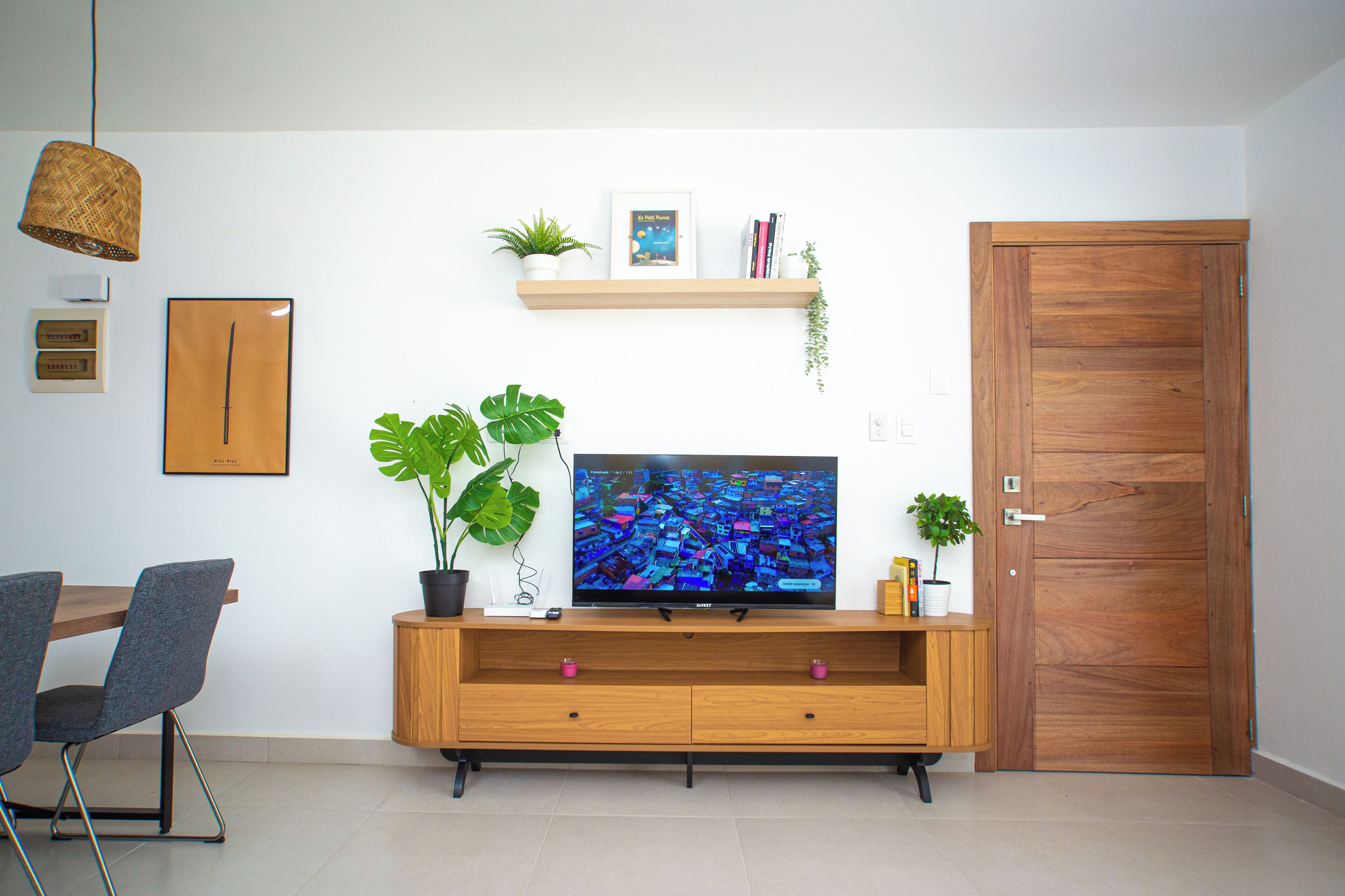 Una sala moderna con un mueble de televisión de madera, un televisor de pantalla plana, dos sillas, una mesa de comedor y una puerta de madera.