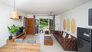 A modern living room with a wooden dining table, a leather sofa, a TV, and a refrigerator. - 0047Cozy 1 bedroom Ocean View  Cabarete (Cabarete)