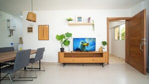 A modern living room with a wooden dining table, grey chairs, a flat-screen TV, and decorative plants. - 0047Cozy 1 bedroom Ocean View  Cabarete (Cabarete)