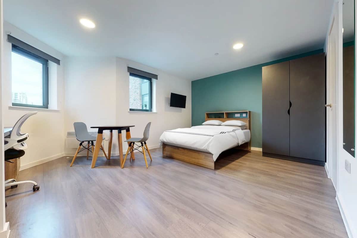 A modern bedroom with a bed, a desk with a chair, and a TV on the wall.