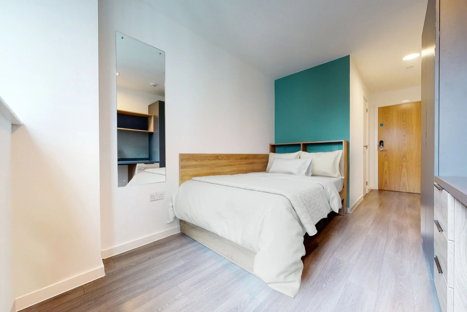 A modern bedroom with a wooden headboard, a large mirror, and a teal accent wall.