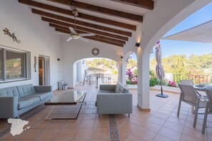 A spacious patio with a ceiling fan, a sofa, a coffee table, and a view of the garden.