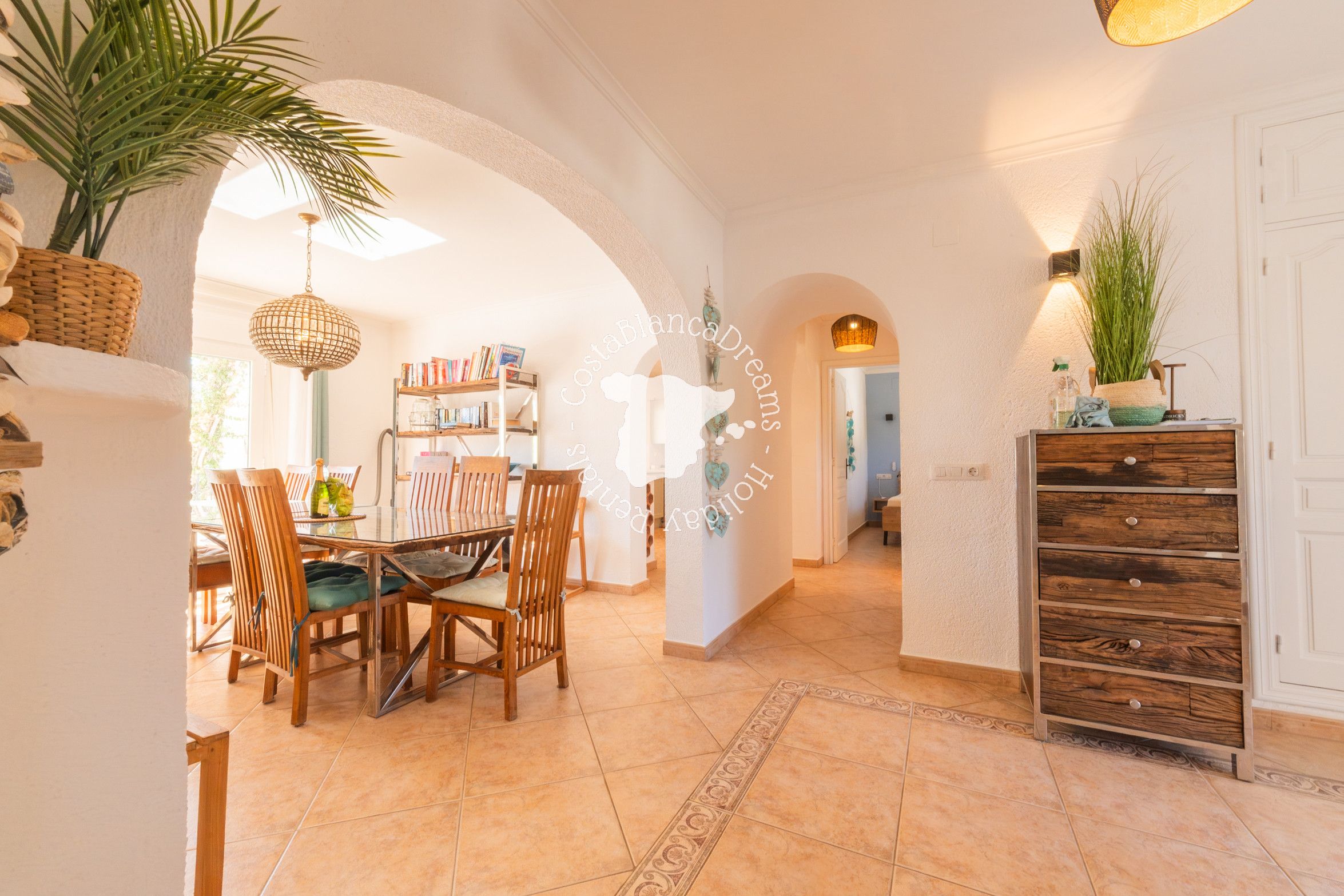 A spacious dining area with a wooden table and chairs, a bookshelf, and a hanging light fixture.