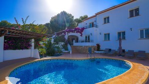 Una piscina amb un voreig de rajola, una pèrgola i un edifici amb balcons i finestres.