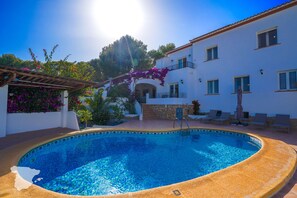 A swimming pool with a tiled edge, a pergola, and a building with balconies and windows.