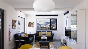 Una sala de estar moderna con un sofá de cuero negro, una mesa de comedor con platos y vasos, y un ventanal con vistas a la montaña.