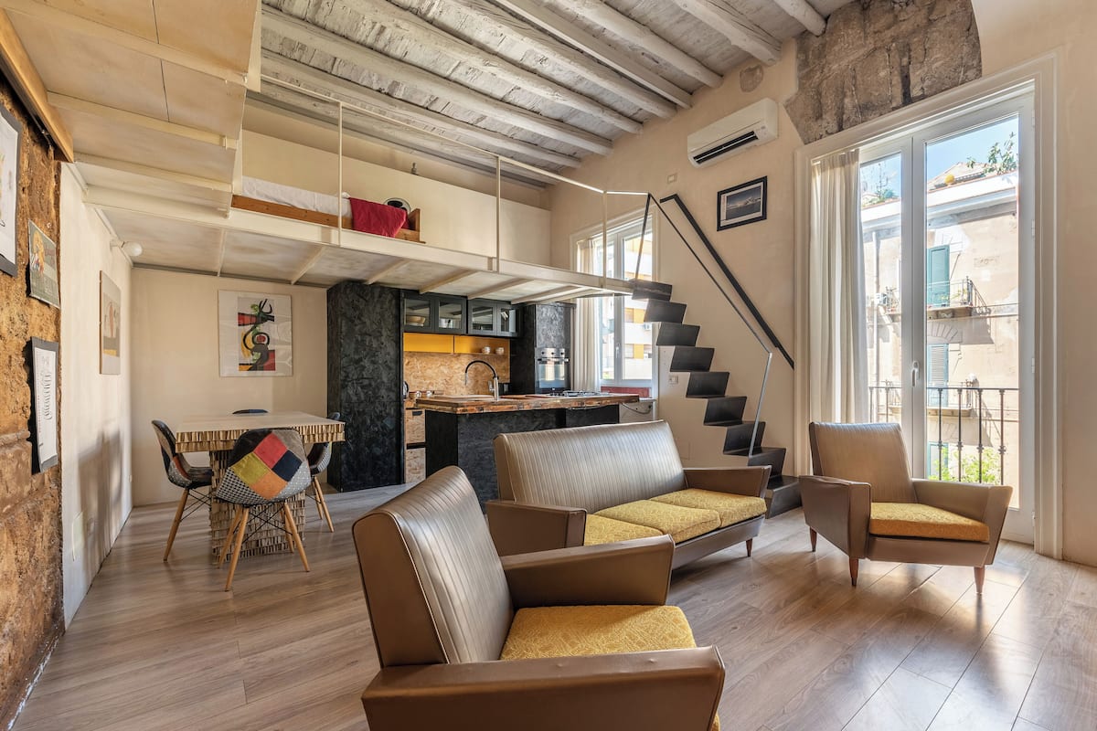 A spacious living area with a high ceiling, a dining table, and a kitchen in the background.
