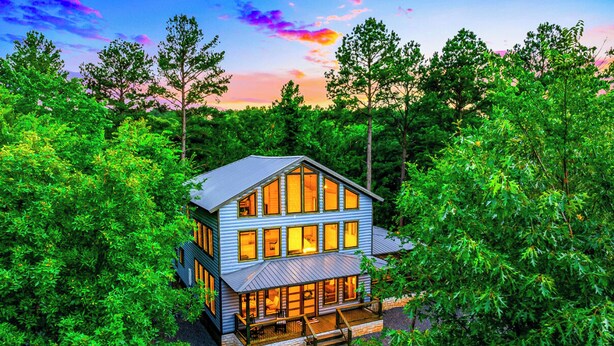 A two-story log cabin with large windows, surrounded by dense forest. - 3BR Forest Hideaway! Playset, Pool Table, Foosball (Broken Bow)
