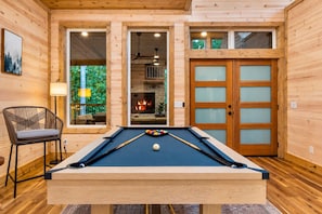 A pool table in a wooden room with a chair, a fireplace, and a door with frosted glass panels. - Playset & Pool Table | Hot Tub | Sleeps 14 (Broken Bow)