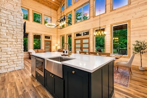 A spacious kitchen with a large island, wooden cabinetry, and a stone accent wall. - Playset & Pool Table | Hot Tub | Sleeps 14 (Broken Bow)