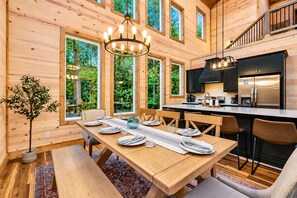 A wooden cabin interior with a dining area, kitchen, and large windows. - Playset & Pool Table | Hot Tub | Sleeps 14 (Broken Bow)